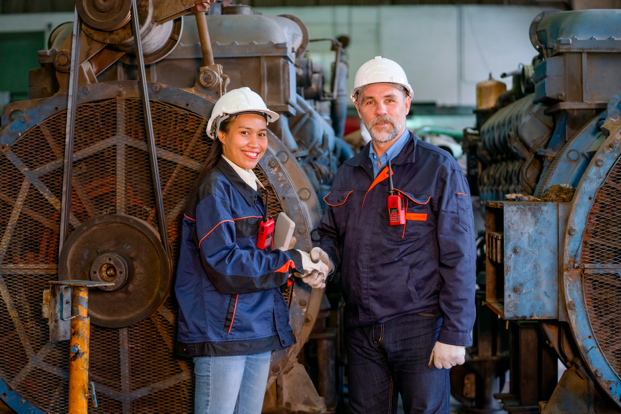 Factory worker or technician stand and shake hands with Asian factory woman in front of big machine